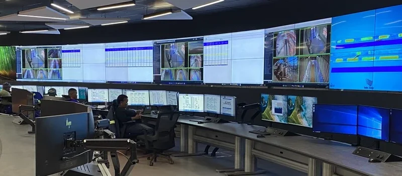 Operators at curved consoles facing a wide video wall in the Khumani mine control room